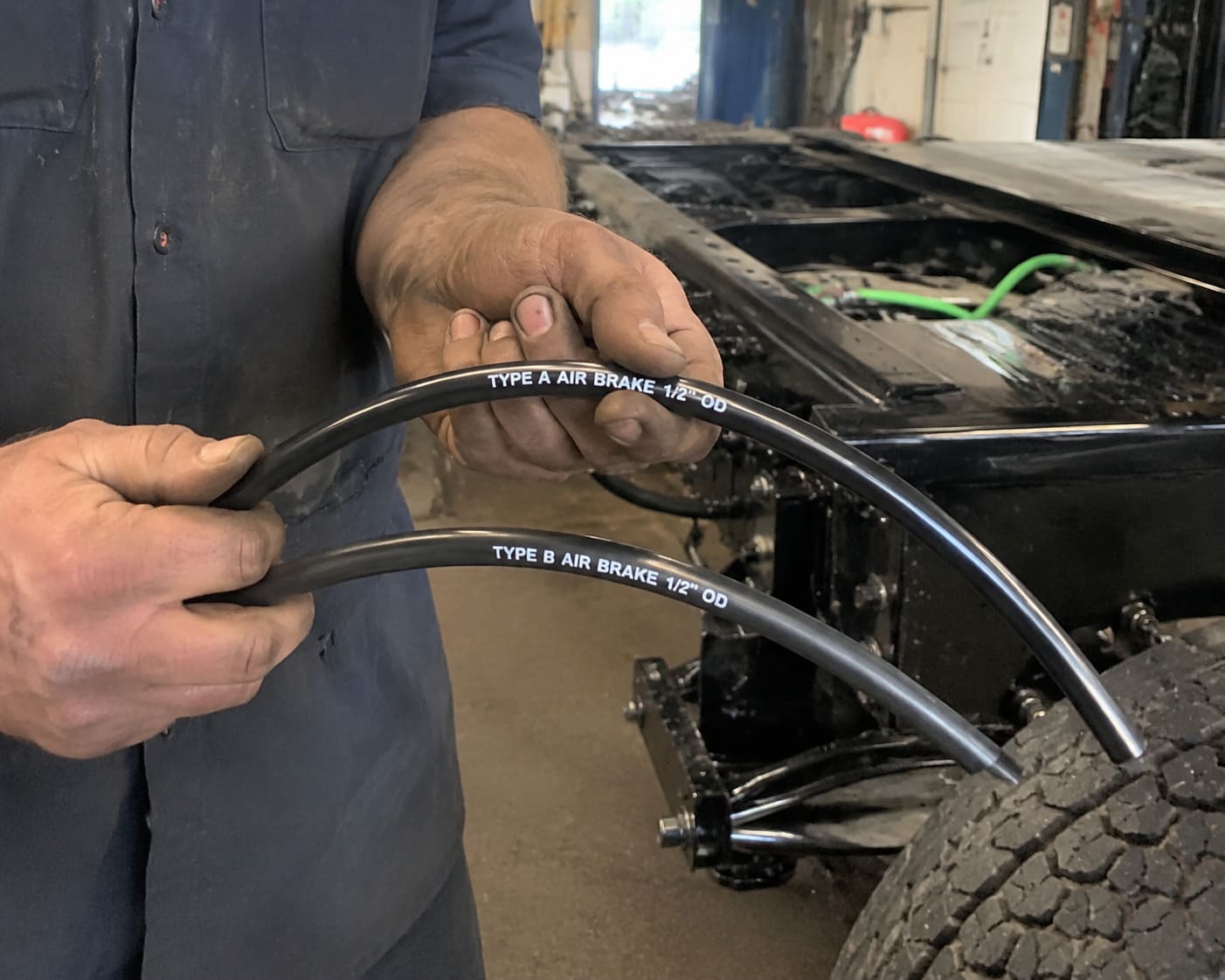 Flexibility difference Type A and Type B air brake tubing a mechanic bending air brake tubing near a truck frame to show difference in flexibility between types
